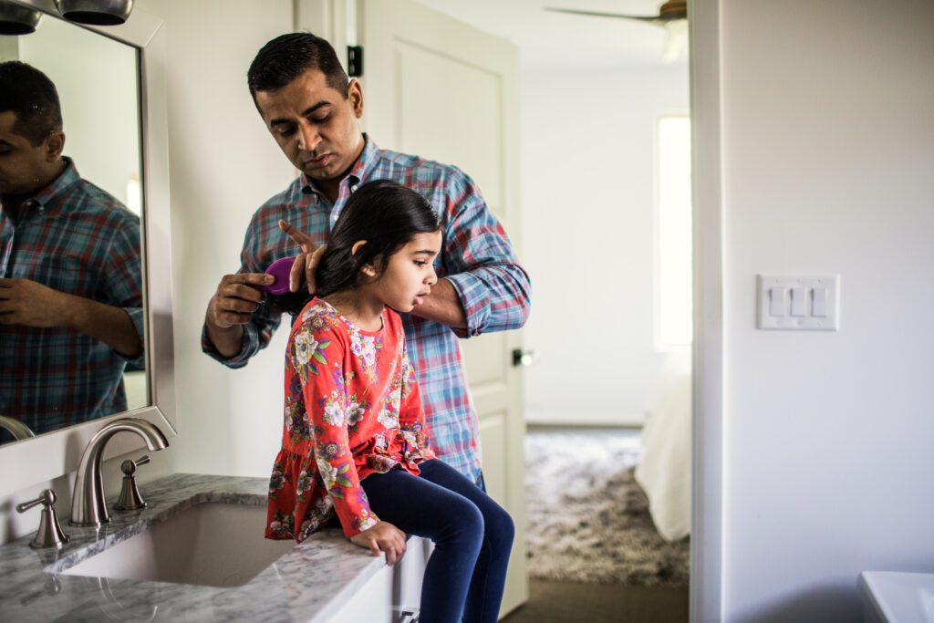 Father brushing daughters hair in bathroom.