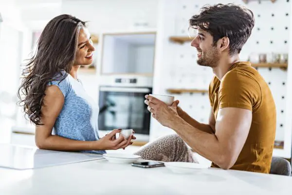 Young happy couple talking while drinking coffee during morning time in the kitchen.