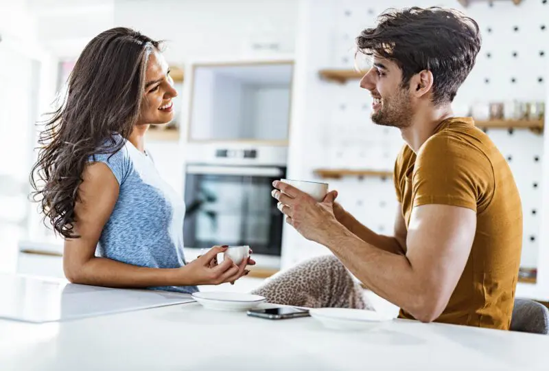 Young happy couple talking while drinking coffee during morning time in the kitchen.