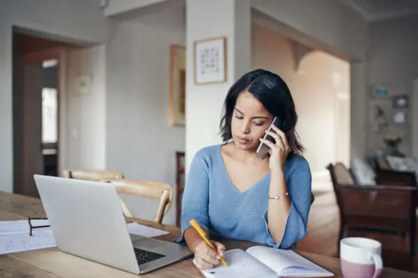 young woman talking on phone, sitting at table with laptop open