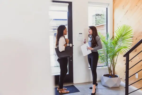 A female real estate agent and a young woman talking at the front door of a home