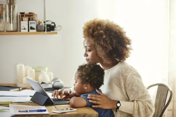 Mother working on tablet with young son sitting on her lap.