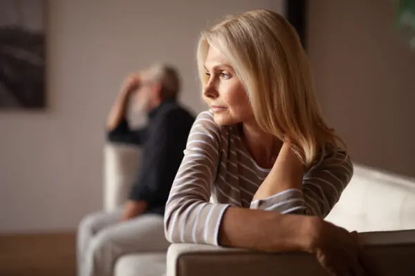 woman looking into distance, husband is behind her looking frustrated