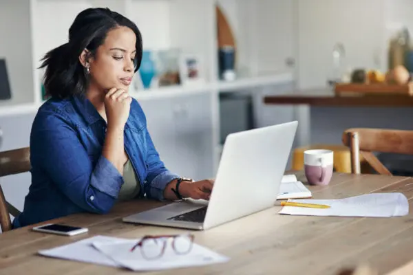 woman looking at laptop while sitting at desk in her home
