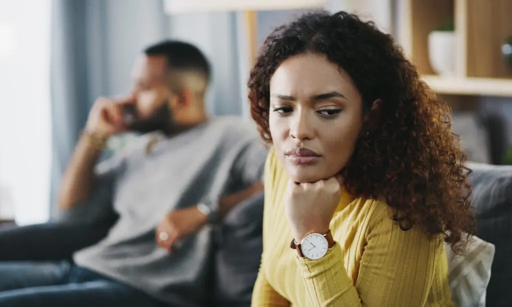 woman sitting on couch, waiting. Husband in background