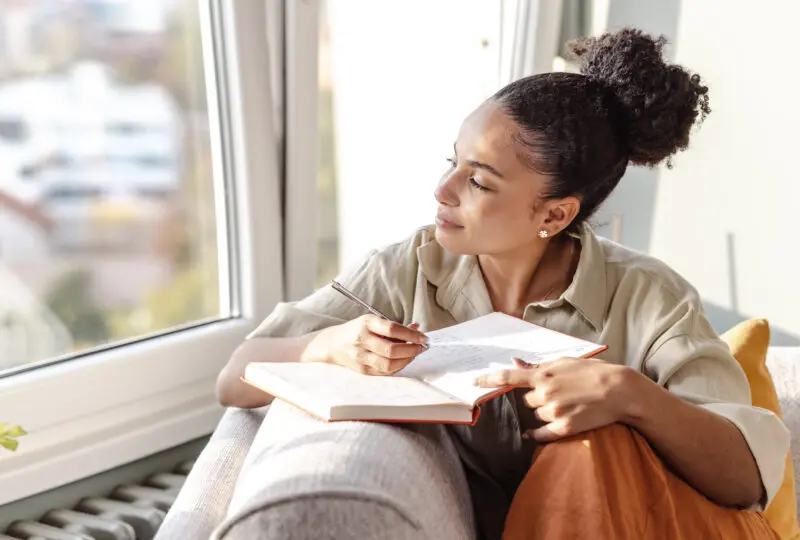 young woman sitting on couch journaling