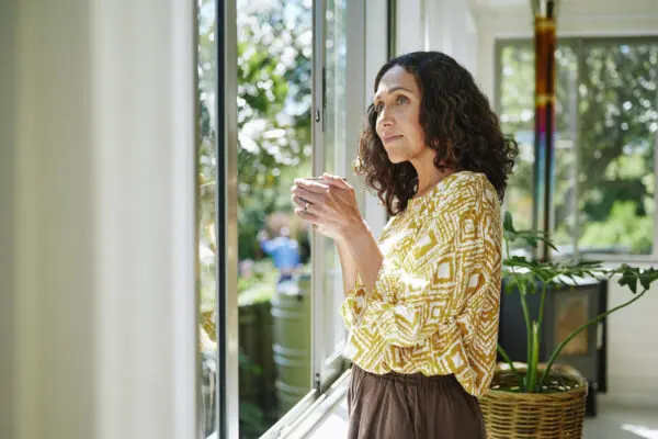 woman with a cup of coffee in her hand, looking out window