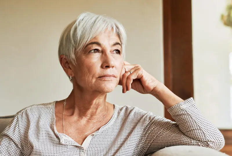 senior women sitting on the couch looking towards a window contemplating divorce