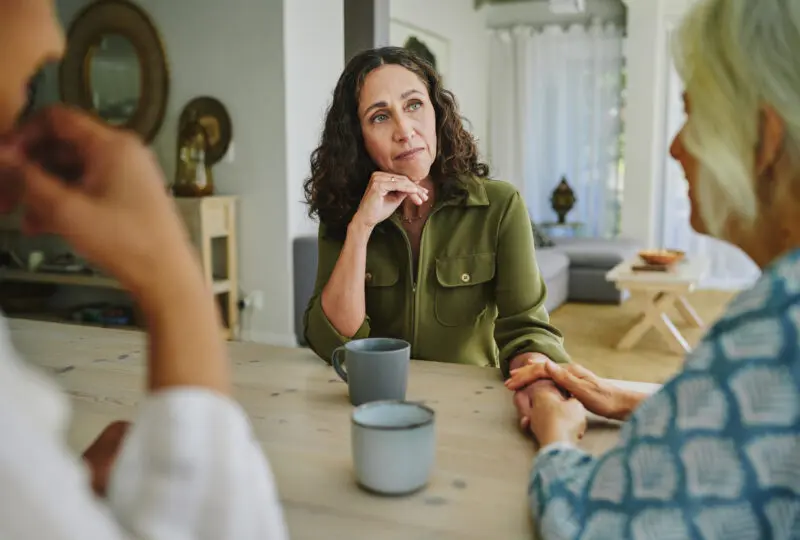 a woman consoling her friend at the kitchen table