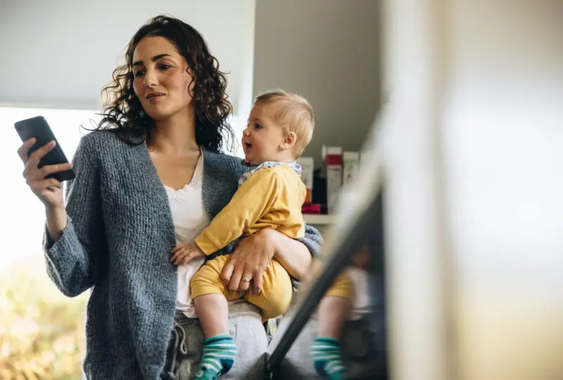 Mother using coparenting app on phone while holding her baby