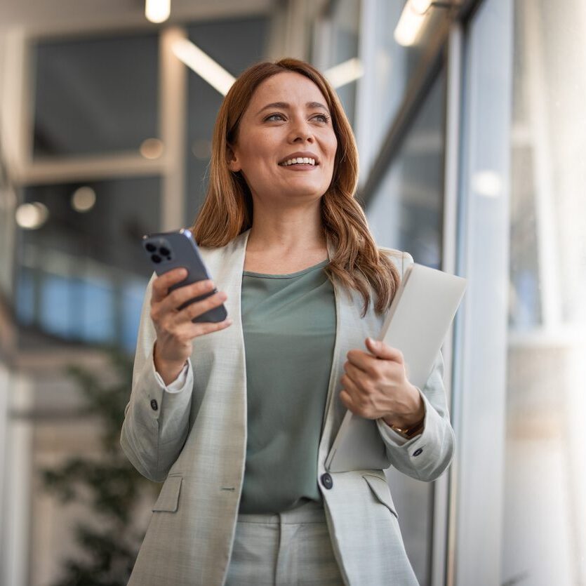 business woman holding phone and laptop in her office