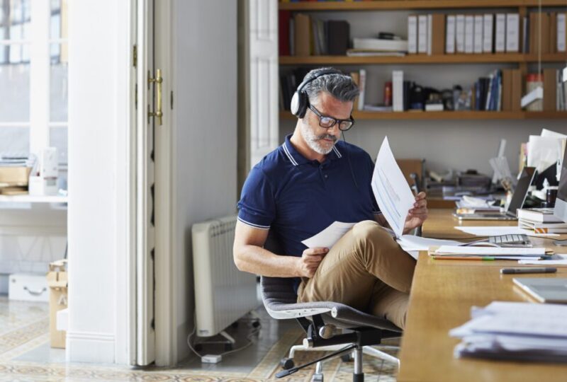 Man sitting in chair at home desk, looking at paperwork