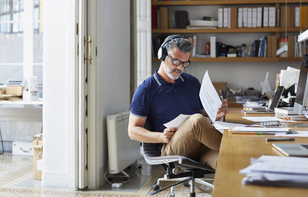 Man sitting in chair at home desk, looking at paperwork