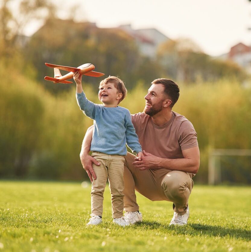 father and son playing with toy airplane in park