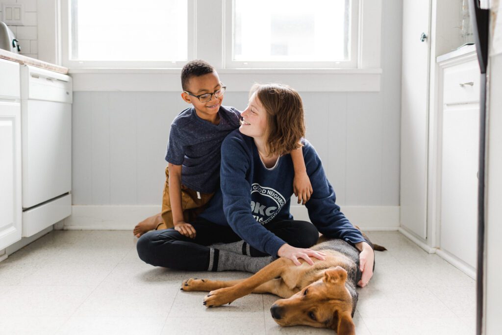 Young boy and mother on the floor smiling at each other while petting their dog.
