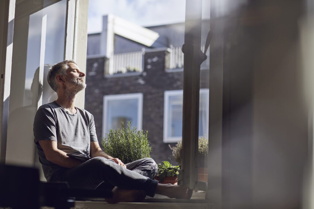 Mature man sitting at the window at home with closed eyes.