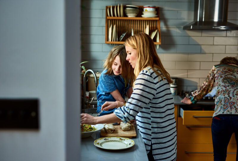 Side view of mother preparing food, daughter sitting on kitchen counter.