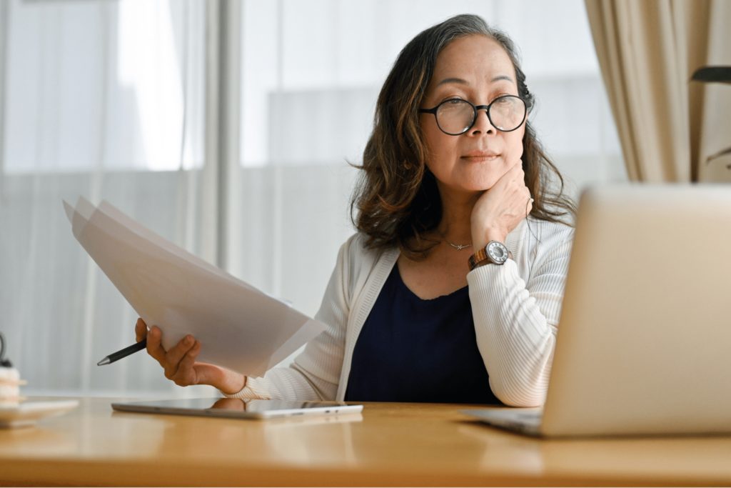 woman looking at computer and holding papers