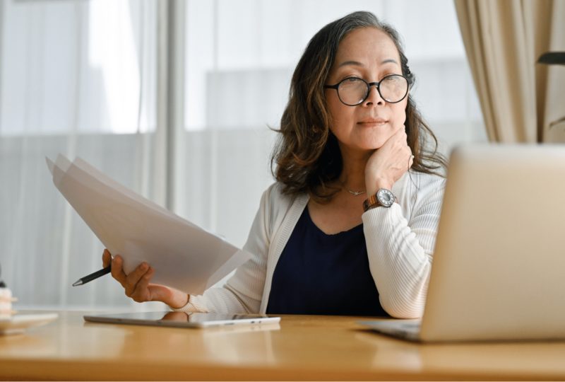 woman looking at computer and holding papers