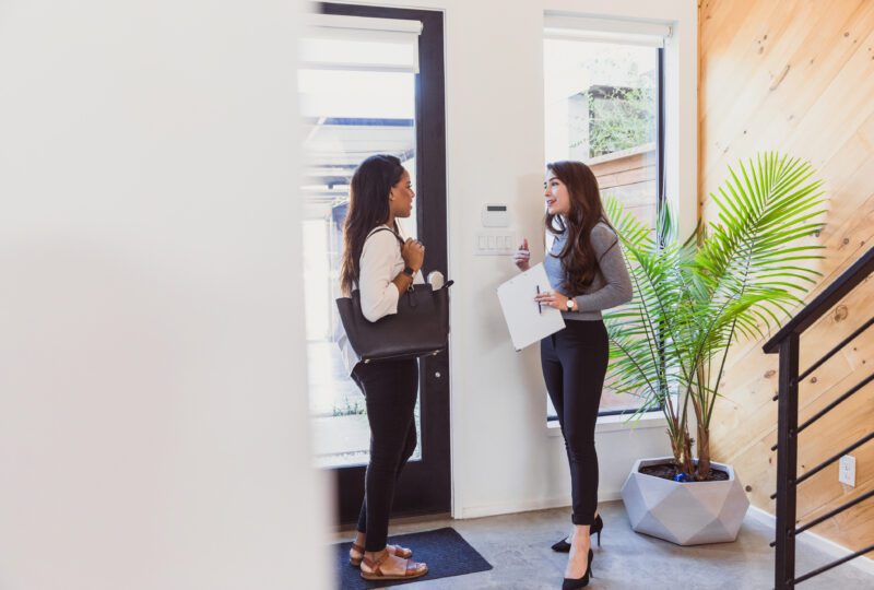 A female real estate agent and a young woman talking at the front door of a home