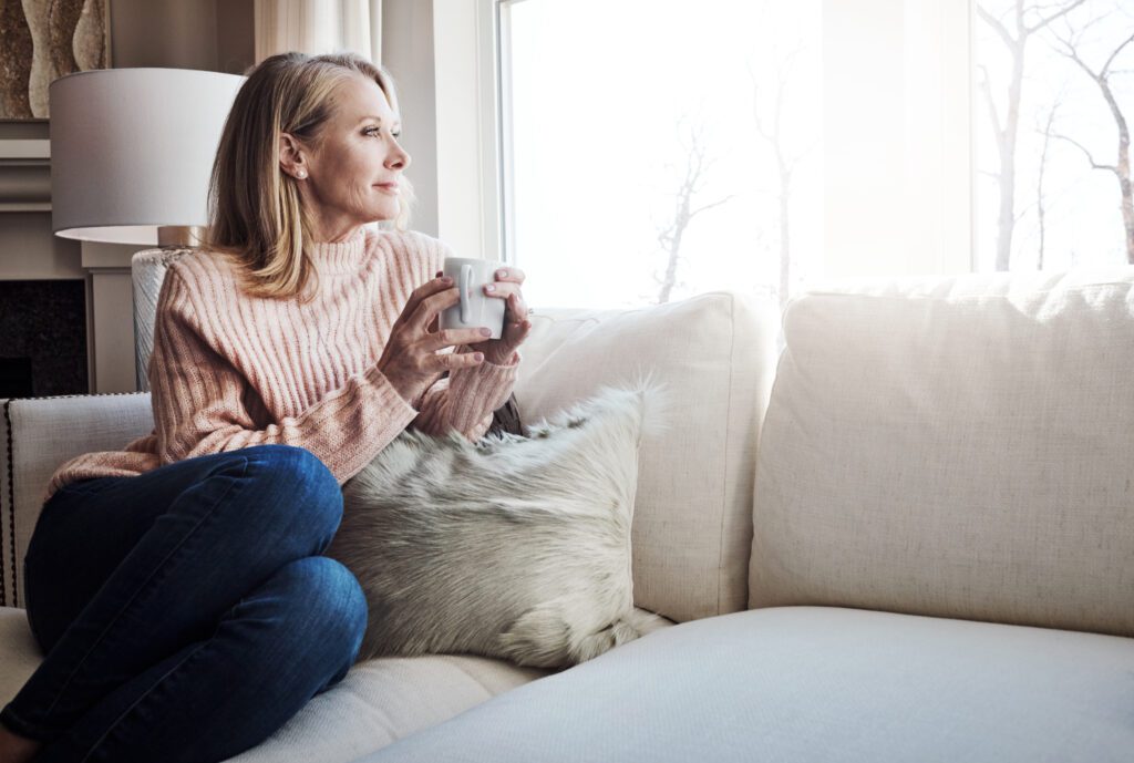 Woman looking out her window at home with a cup of coffee