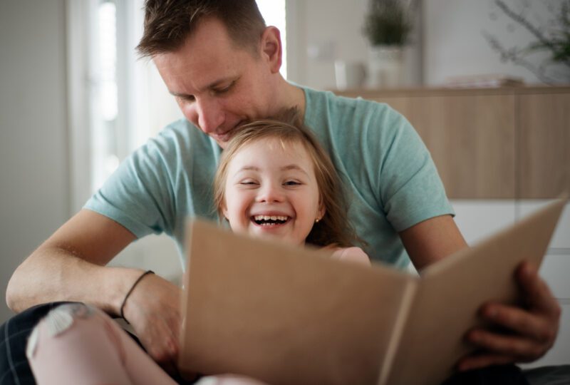 Daughter smiling, dad looking down at her wearing blue shirt