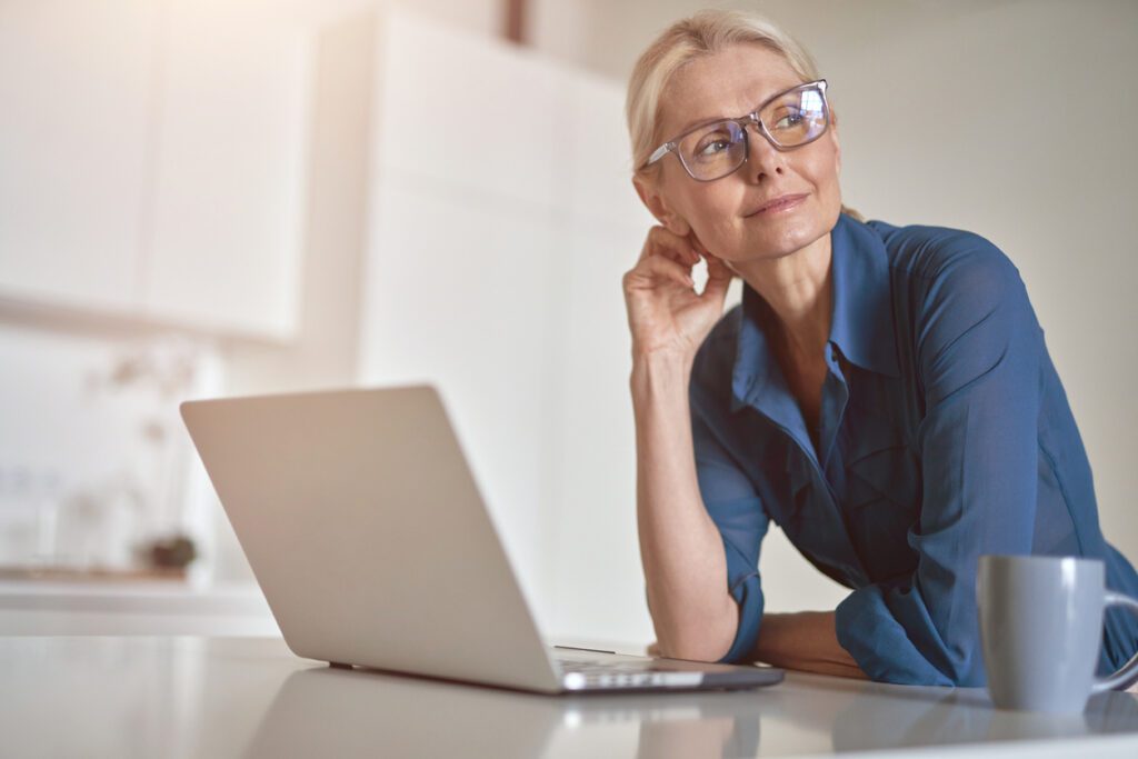 middle aged woman with laptop at desk looking away from it