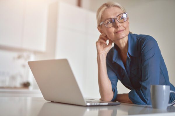 middle aged woman with laptop at desk looking away from it