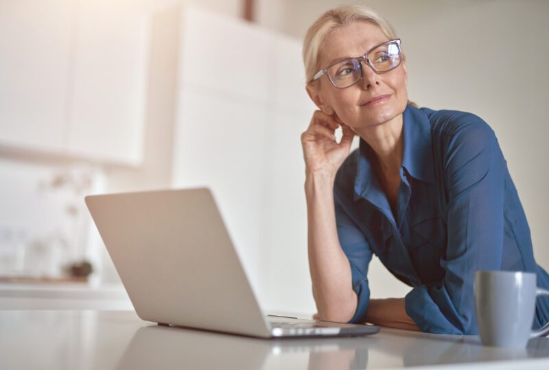 middle aged woman with laptop at desk looking away from it