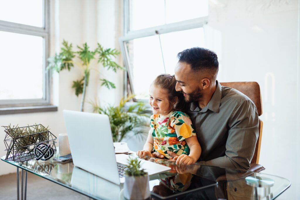 Businessman in office with young daughter looking at his laptop