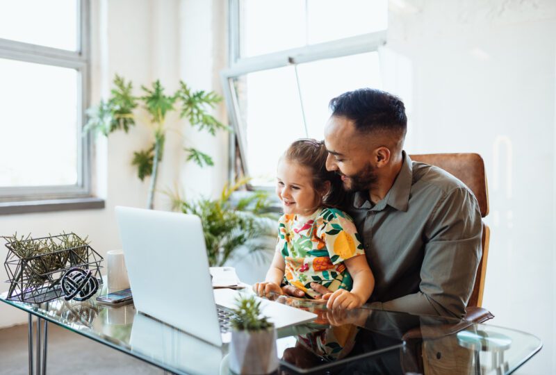 Businessman in office with young daughter looking at his laptop