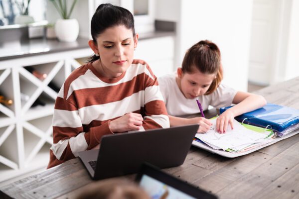 Mother working on laptop while daughter does homework at the dining room table