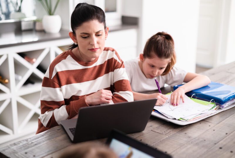 Mother working on laptop while daughter does homework at the dining room table