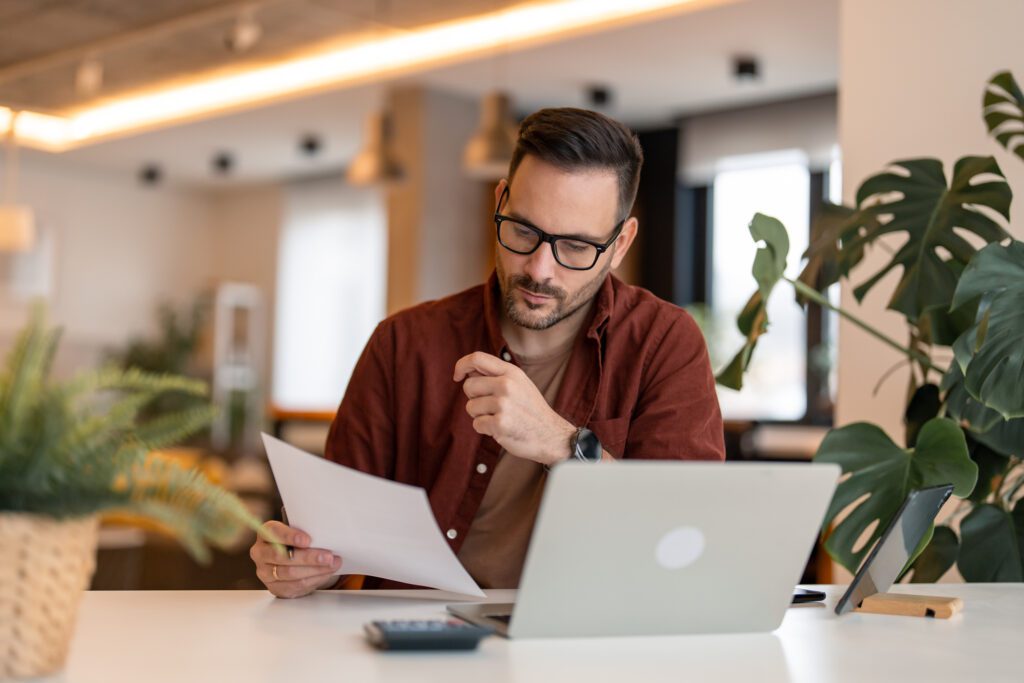 male business owner looking at paperwork and laptop