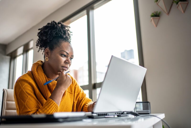 Women wearing a yellow sweater and looking at her laptop at her desk at home.