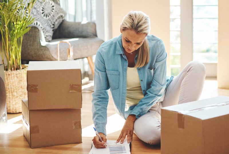 woman sitting on floor with moving boxes and a checklist