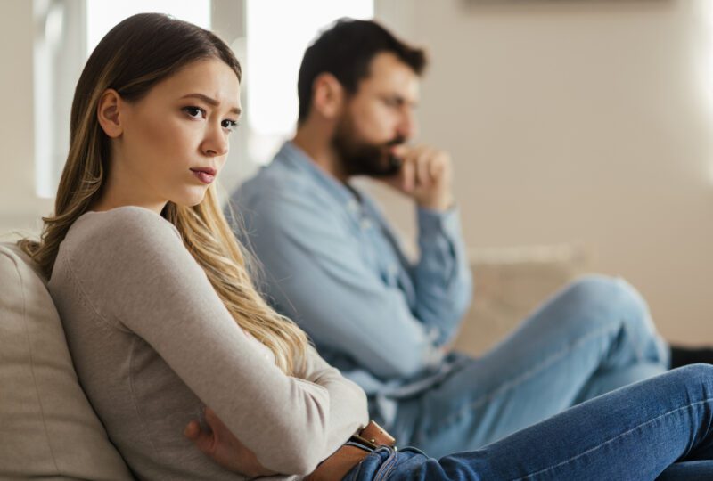 Young sad woman sitting on sofa having relationship difficulties with her spouse
