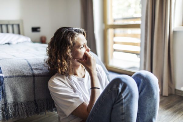 young adult woman sitting at home along, looking out window