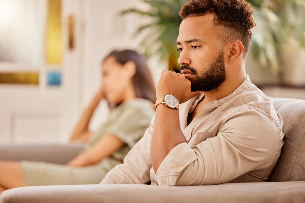 couple sitting on couch far apart from each other looking concerned