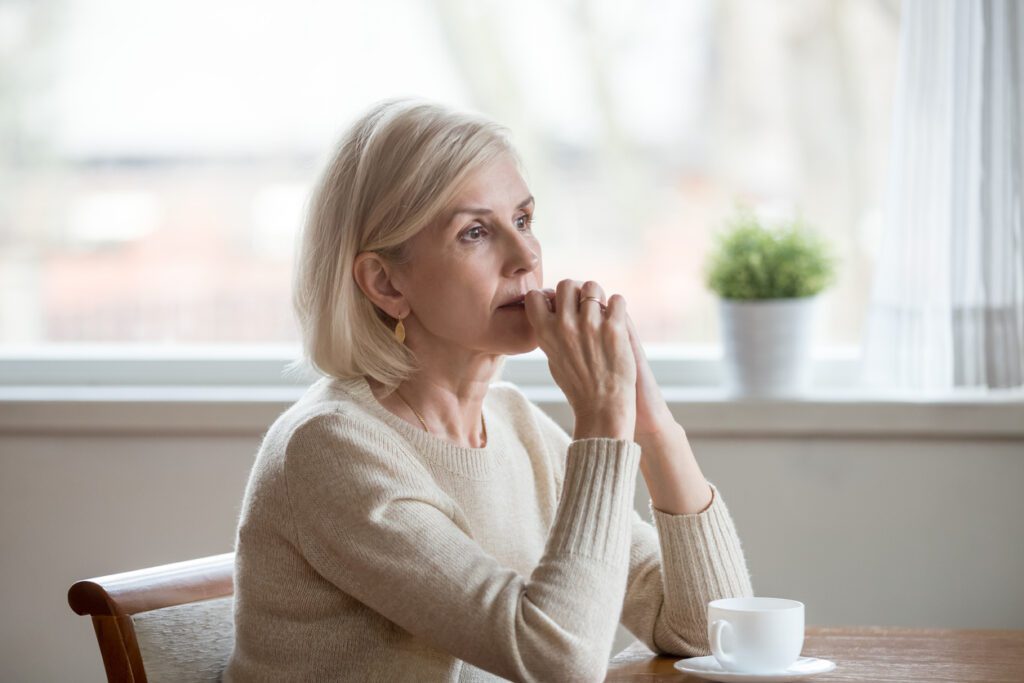 mature woman sitting at kitchen table, deep in thought