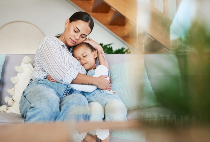 mother and daughter sitting on couch, hugging