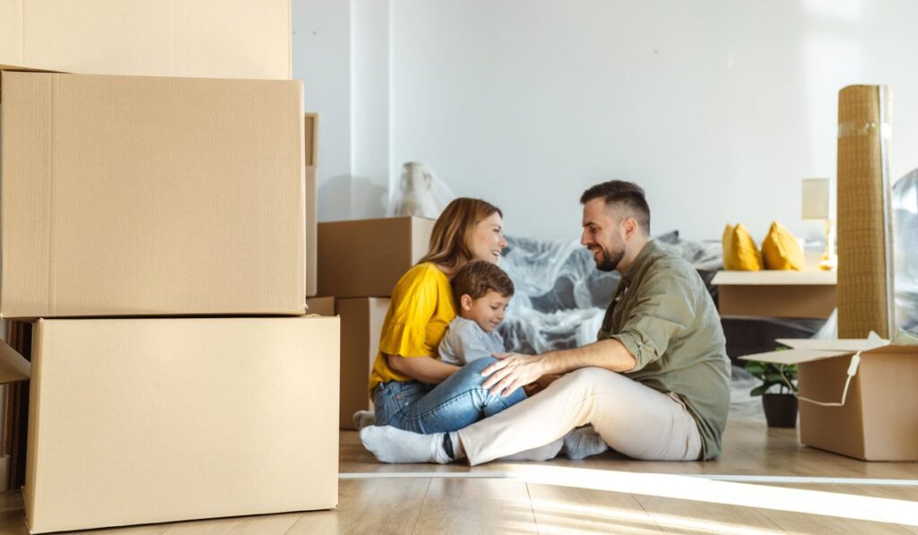 happy family sitting on the floor of their new home with moving boxes around them