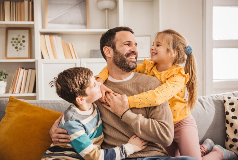 dad with his children, all smiling while sitting on the couch
