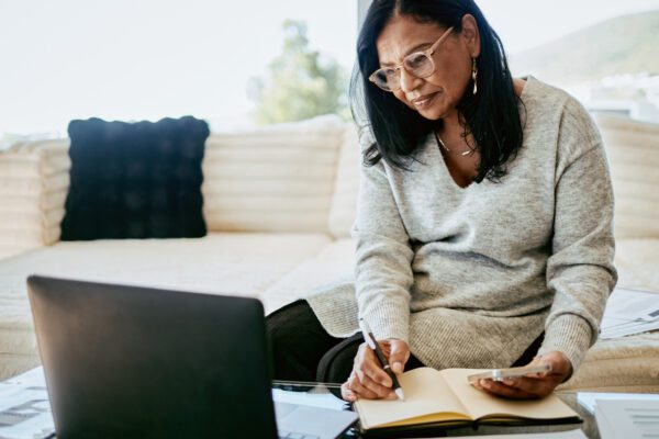 middle aged women at home looking at laptop and taking notes