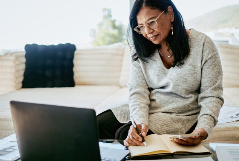 middle aged women at home looking at laptop and taking notes