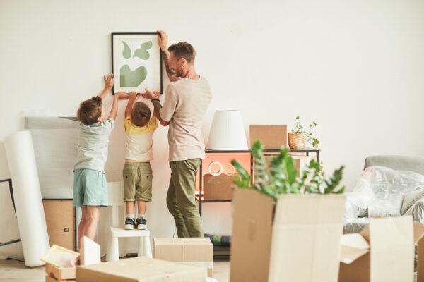 a father hanging a photo on the wall with the help of his two sons